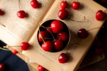 Naklejka na ściany i meble Atmospheric photo of ripe red sweet cherries and books on the rustic wooden background. Selective focus. Shallow depth of field.