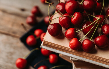 Atmospheric photo of ripe red sweet cherries and books on the rustic wooden background. Selective focus. Shallow depth of field.