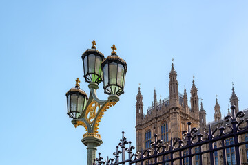 Decorative street light and wrought iron railings outside of the Houses of Parliament, London, UK. Blue sky background with space for text
