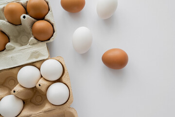 Top view of eggs in shells near carton boxes on white background.