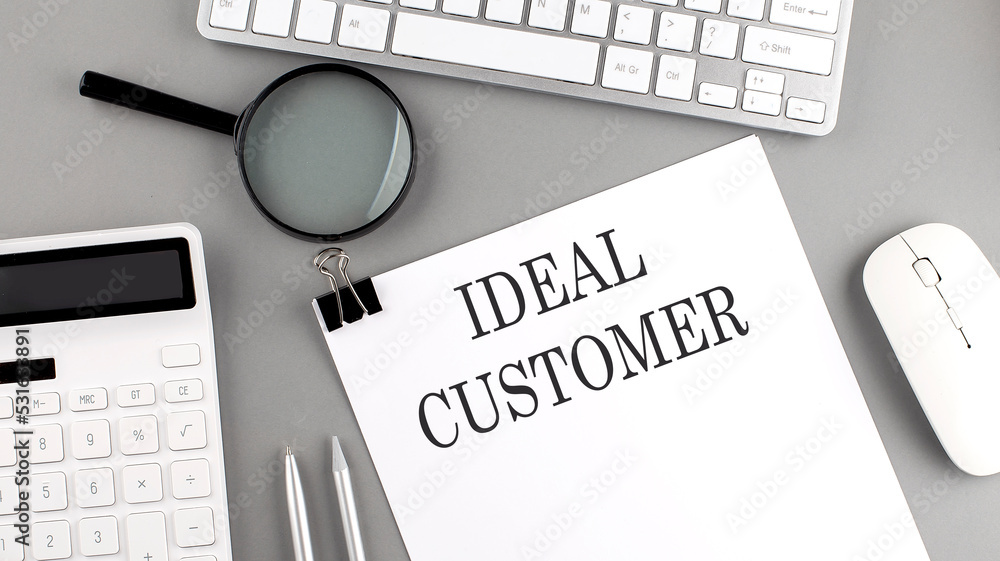 Aufkleber ideal customer written on paper with office tools and keyboard on the grey background