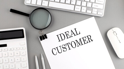 IDEAL CUSTOMER written on paper with office tools and keyboard on the grey background