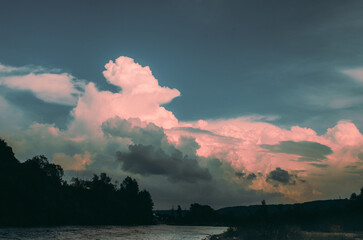 Beautiful cloudy sky at sunset over the river. The high bank of the river is overgrown with grass.