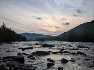 Obraz premium Beautiful cloudy sky at sunset over the river. The high bank of the river is overgrown with grass.