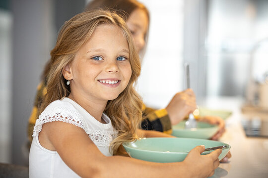 Portrait of little girl eating in kitchen with her sister in bacground