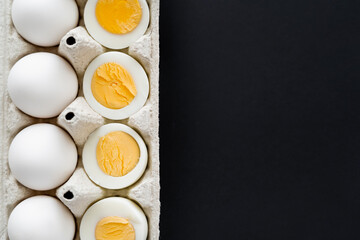 Top view of cut boiled and raw eggs in carton container isolated on black.