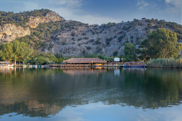 Fototapeta premium The rock-cut temple tombs of the ancient city of Kaunos in Dalyan, Muğla, Turkey. Beautiful view of Dalyan river with reed beds, excursion boats and carved tombs in the background.