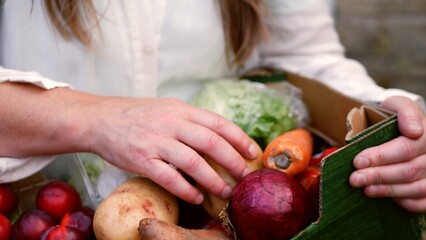 Selecting groceries from box of fresh vegetables and fruit 
