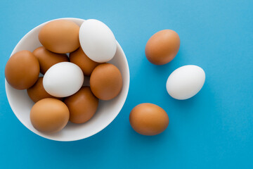 Top view of brown and white eggs in bowl on blue background.