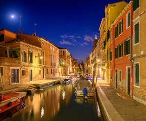 Night panorama of narrow cozy streets of the canals with parked boats in Venice, Italy. Architecture and landmark of Venice.