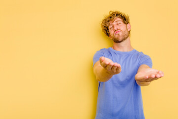 Young caucasian man isolated on yellow background folding lips and holding palms to send air kiss.