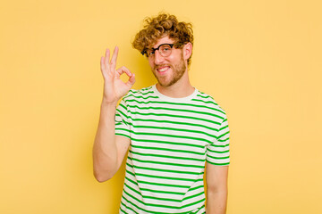 Young caucasian man isolated on yellow background cheerful and confident showing ok gesture.