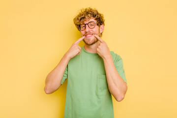 Young caucasian man isolated on yellow background smiles, pointing fingers at mouth.