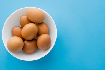 Top view of chicken eggs in bowl on blue background.
