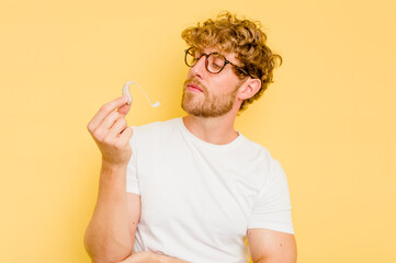 Young caucasian man wearing hearing aid isolated on yellow background