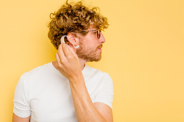 Young caucasian man wearing hearing aid isolated on yellow background - Powered by Adobe