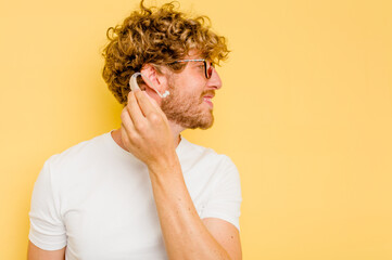 Young caucasian man wearing hearing aid isolated on yellow background