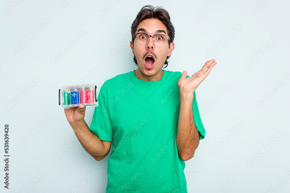 Wall mural young hispanic man holding battery box isolated on white background surprised and shocked.