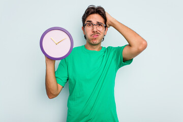 Young hispanic man holding a clock isolated on white background being shocked, she has remembered important meeting.