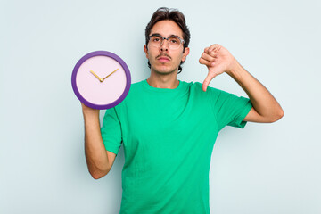 Young hispanic man holding a clock isolated on white background showing a dislike gesture, thumbs...