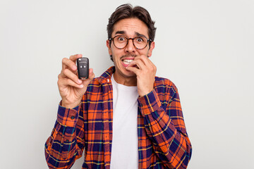 Young hispanic man holding car keys isolated on white background biting fingernails, nervous and...