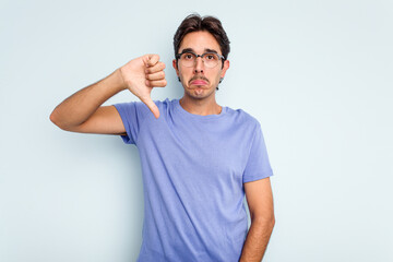 Young hispanic man isolated on blue background showing a dislike gesture, thumbs down. Disagreement...