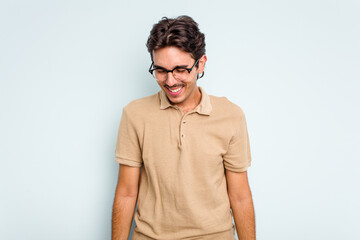 Young hispanic man isolated on blue background laughs and closes eyes, feels relaxed and happy.