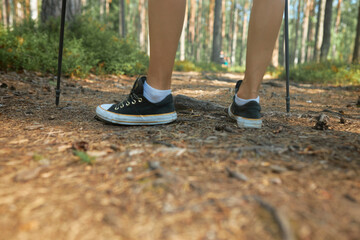 Cropped shot of feet woman or teenager hiker in black sneakers hiking in forest using nordic walking sticks. Tourist in wild nature. Summer camping and leisure activity on fresh air