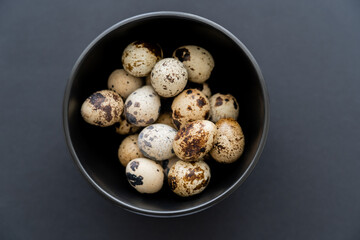 Top view of fresh quail eggs in bowl on black background.