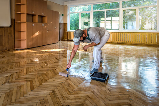 Lacquering parquet floors. Worker uses a roller to coating floors. Varnishing lacquering parquet floor by paint roller - second layer