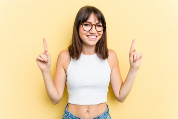 Young caucasian woman isolated on yellow background indicates with both fore fingers up showing a...