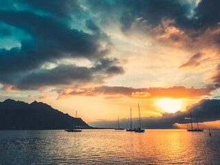 Fototapeta na wymiar Majestic yacht tour travel landscape. Dramatic nature sunset in tropical island lagoon. Yachts silhouette against bright orange sun and blue clouds sky. Wonderful picturesque scene. French Polynesia