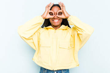 Young African American woman with braids hair isolated on blue background showing okay sign over eyes