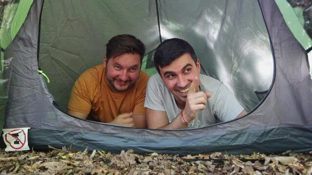 Two friends lying in a tent laughing and mocking while pointing with fingers