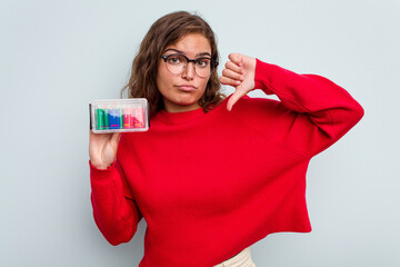 Naklejka premium Young caucasian woman holding battery box isolated on blue background showing a dislike gesture, thumbs down. Disagreement concept.