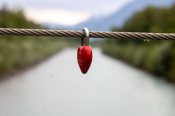 Rotes Herz aus Metall auf dem Brucke hängen lassen als zeichen von Liebe,in Hintergrund Fluss und Wald blurred,geschlossene Liebe,Liebe für immer