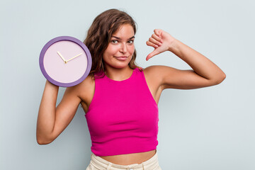 Young caucasian woman holding a clock isolated on blue background feels proud and self confident, example to follow.