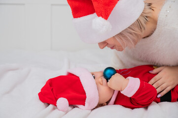 Caucasian woman hugging baby son in santa claus costume. 