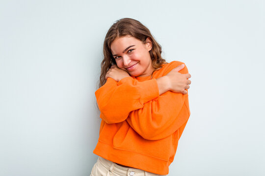 Young caucasian woman isolated on blue background hugs, smiling carefree and happy.