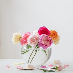 beautiful roses in round glass vase on white background