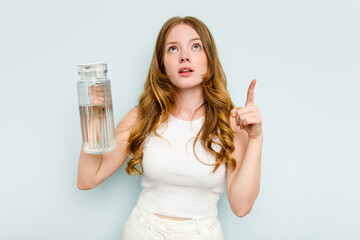 Young caucasian woman holding jar of water isolated on blue background pointing upside with opened mouth.