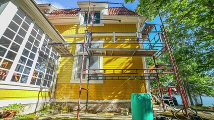 Low angle shot of renovation workers repainting yellow color on an old wooden cottage in timelapse.