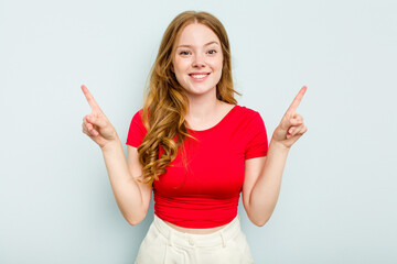 Young caucasian woman isolated on blue background indicates with both fore fingers up showing a...