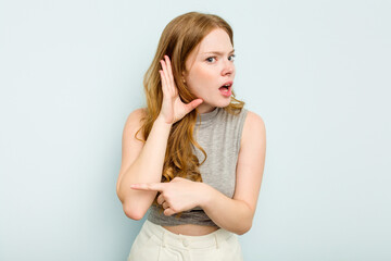 Young caucasian woman isolated on blue background trying to listening a gossip.