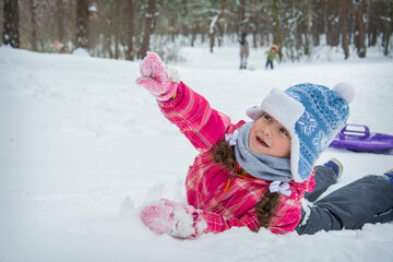 In the winter forest on the snow lies a little funny girl. Winter entertainment for children.