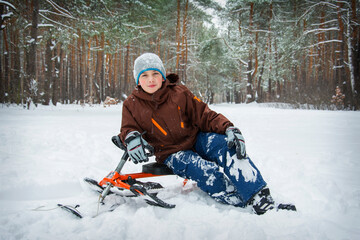 Fototapeta na wymiar In the winter forest, a boy is sitting on a snowmobile. Winter entertainment for children.
