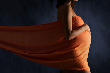 Pregnant woman wrapped in a orange drape on blue background
