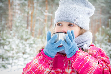 little beautiful girl drinks hot drink in winter park