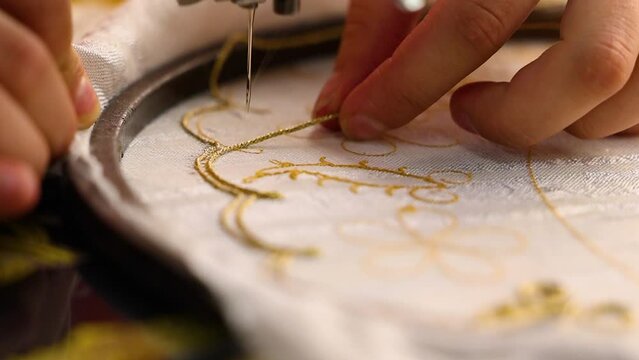 Woman sewing with a machine an embroidery with golden strings