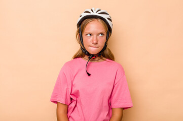 Little caucasian girl wearing a bike helmet isolated on beige background confused, feels doubtful and unsure.